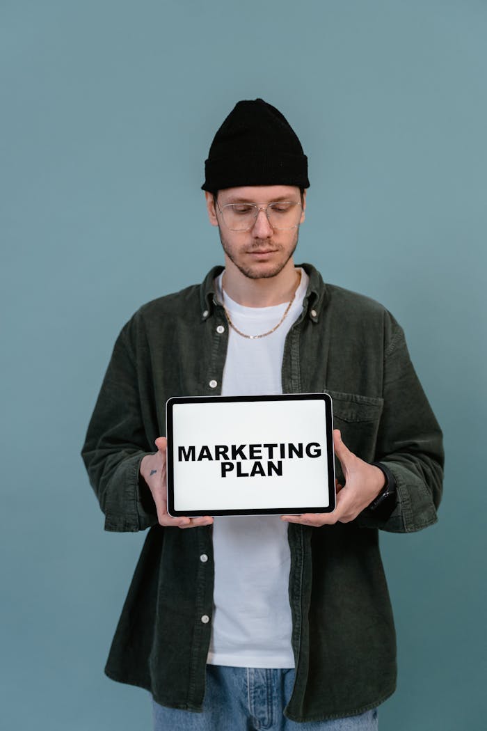 ours-journey Adult wearing casual clothing holding a tablet that reads 'Marketing Plan'.